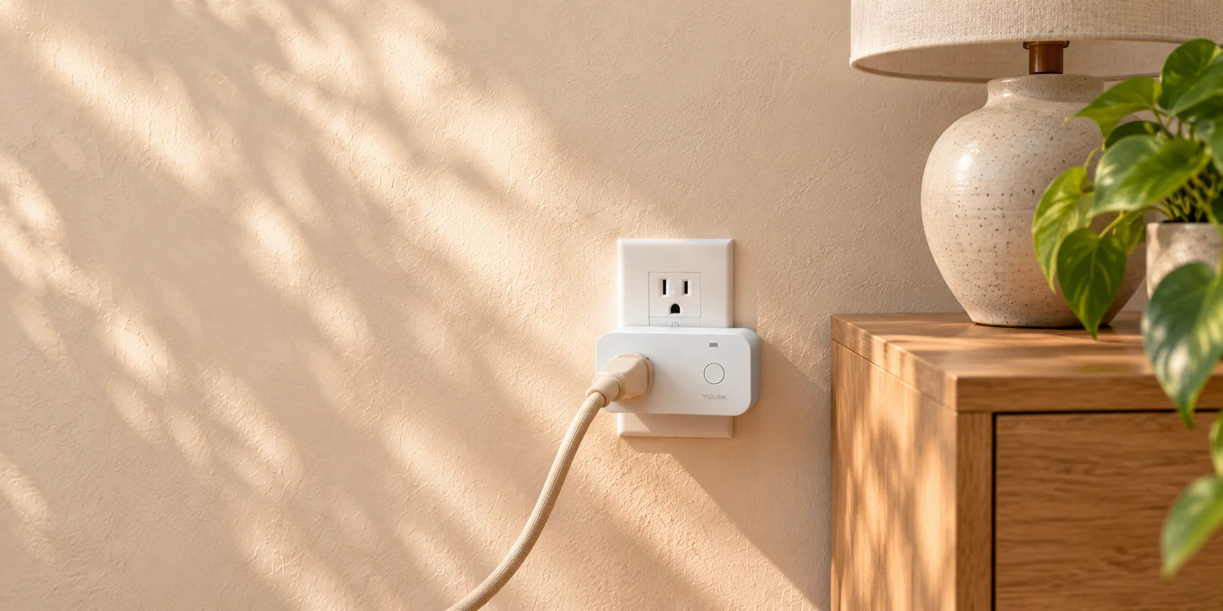 YoLink smart plug with power monitoring beside an unlit lamp and a leafy plant in natural daylight